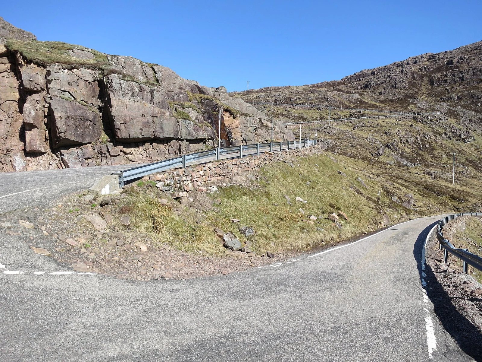 Een scherpe haarspeldbocht van de Bealach na Bà tussen rotswanden, grashellingen en vangrails.