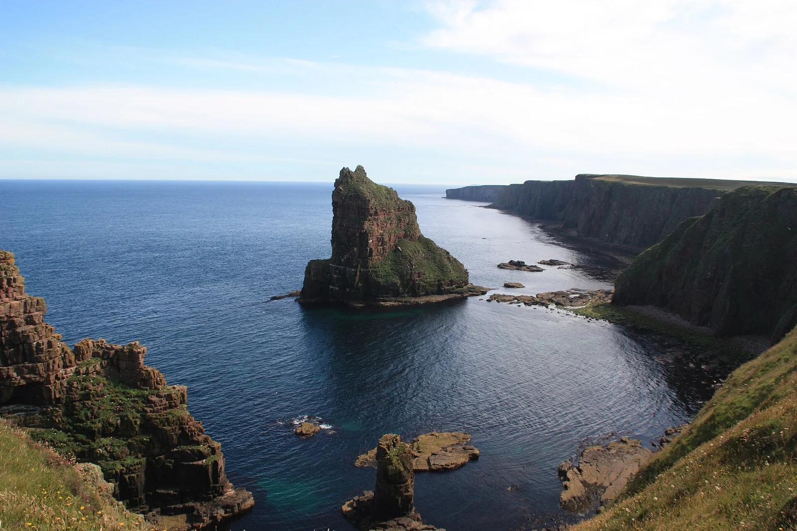 Een hoge puntige zeestapel voor de kliffen van Duncansby Head, omgeven door donkerblauw zeewater.