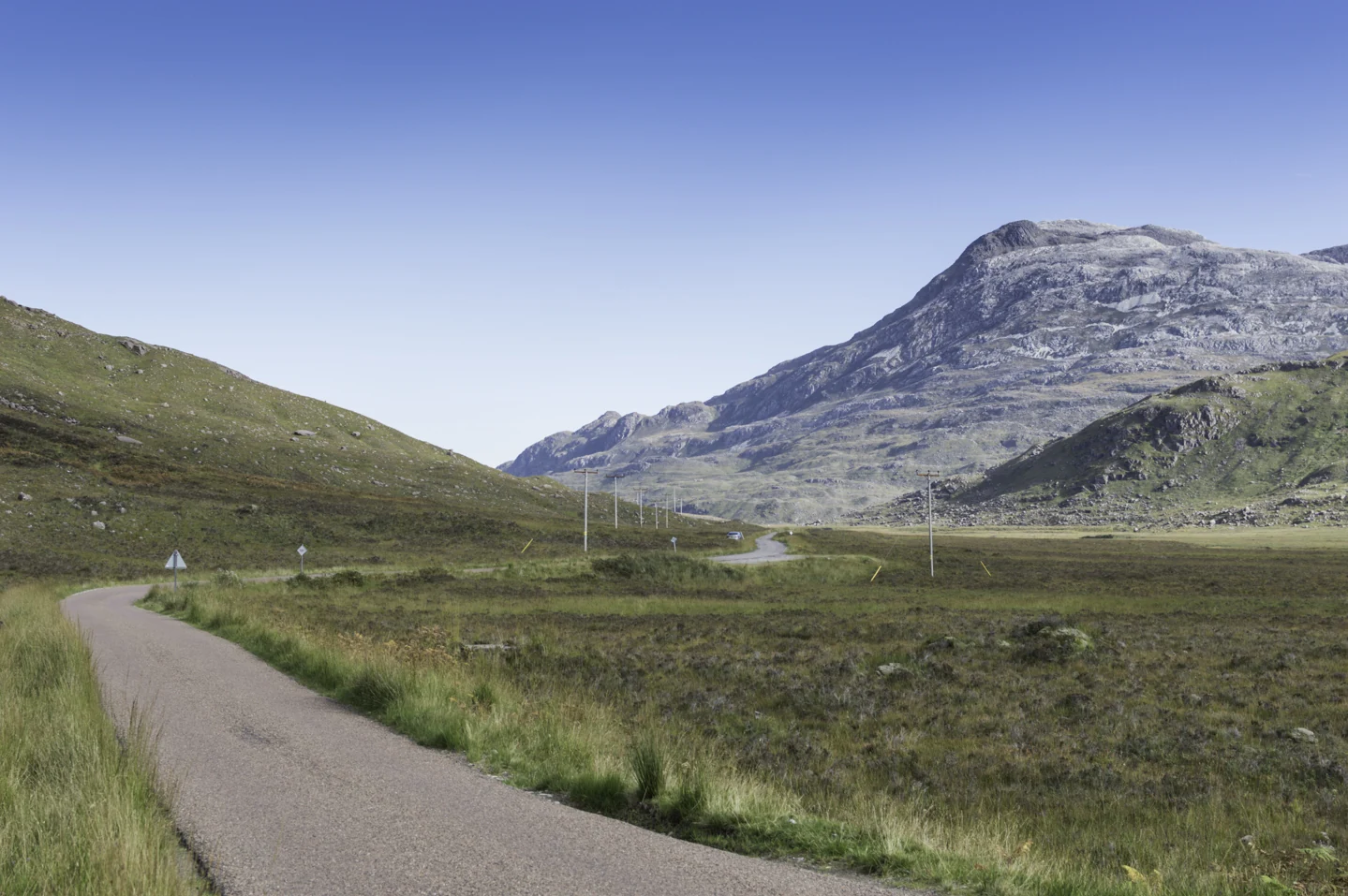 Een smalle weg slingert door Glen Torridon naar een gelaagde bergwand onder blauwe lucht.
