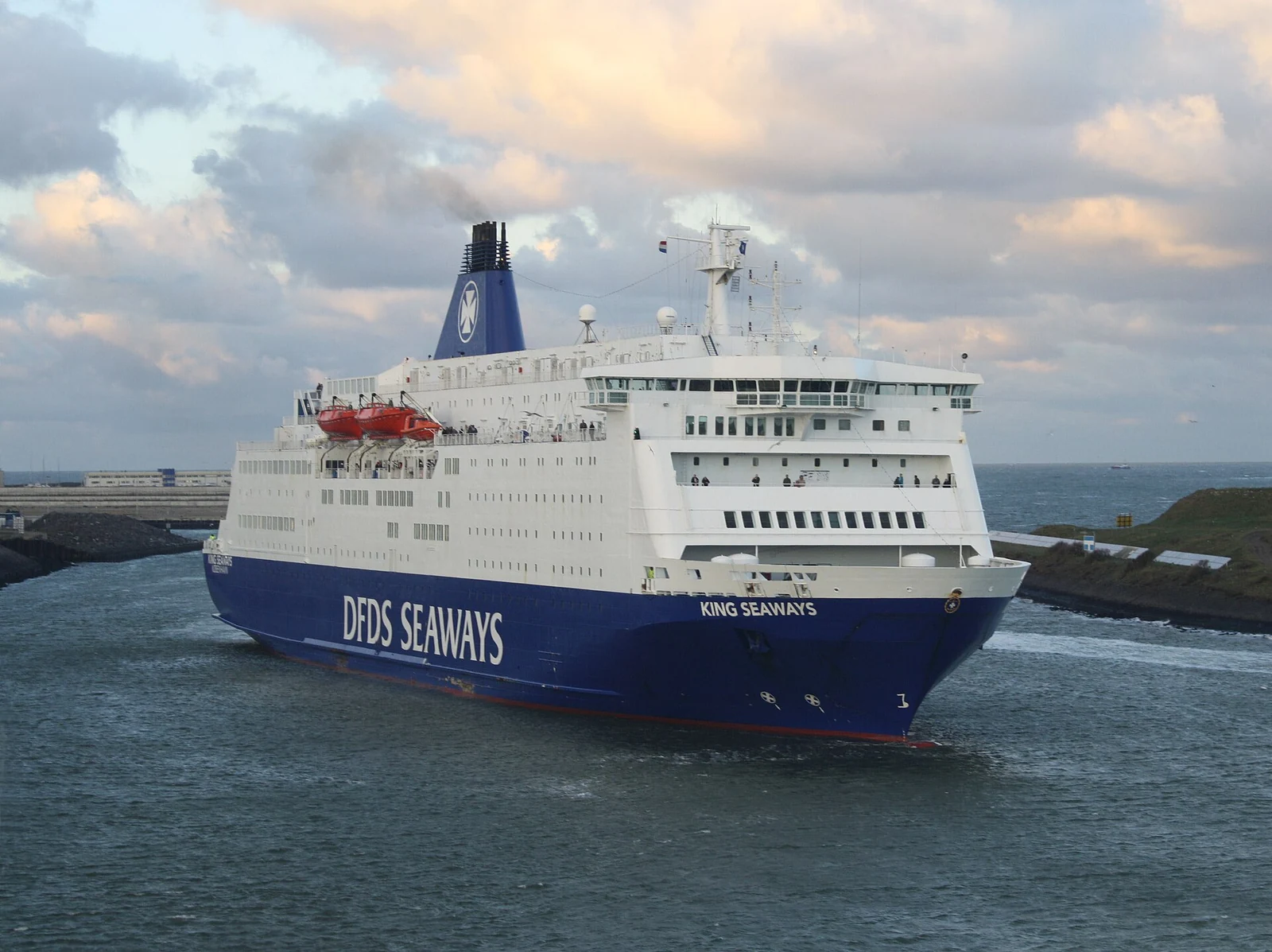 De wit-blauwe DFDS-ferry King Seaways vaart tussen de havenhoofden van IJmuiden onder een bewolkte lucht.