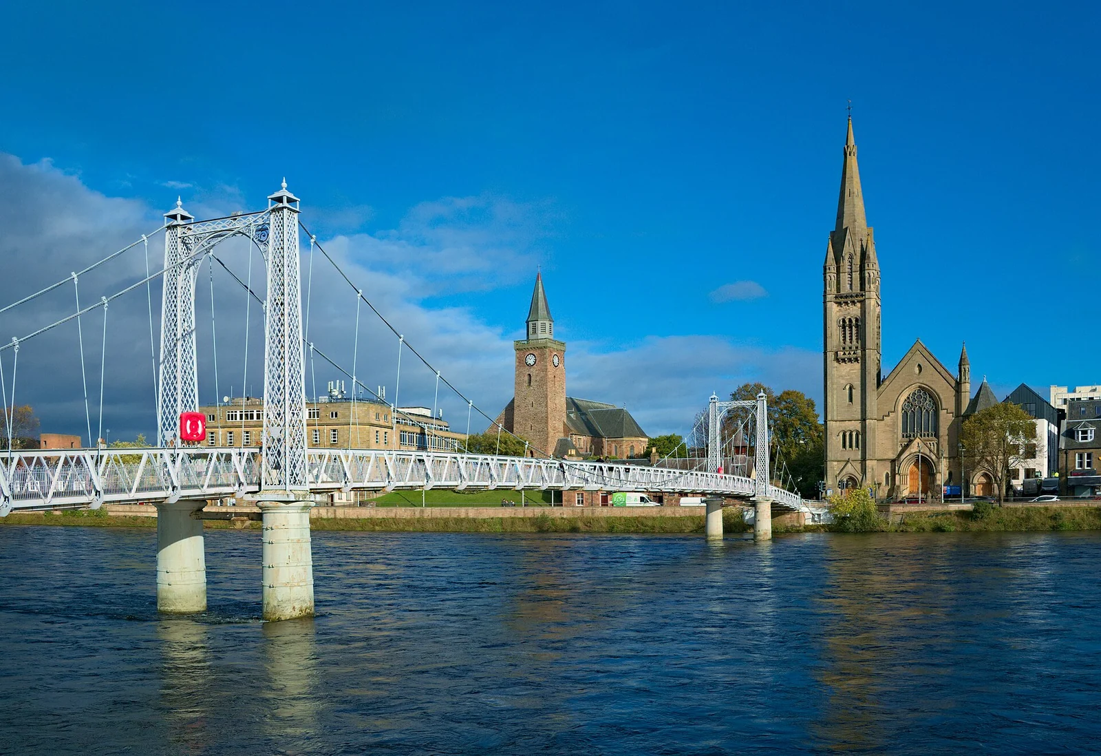 De witte hangbrug over de River Ness in Inverness, met kerktorens aan de overkant en weerspiegelingen in het water.